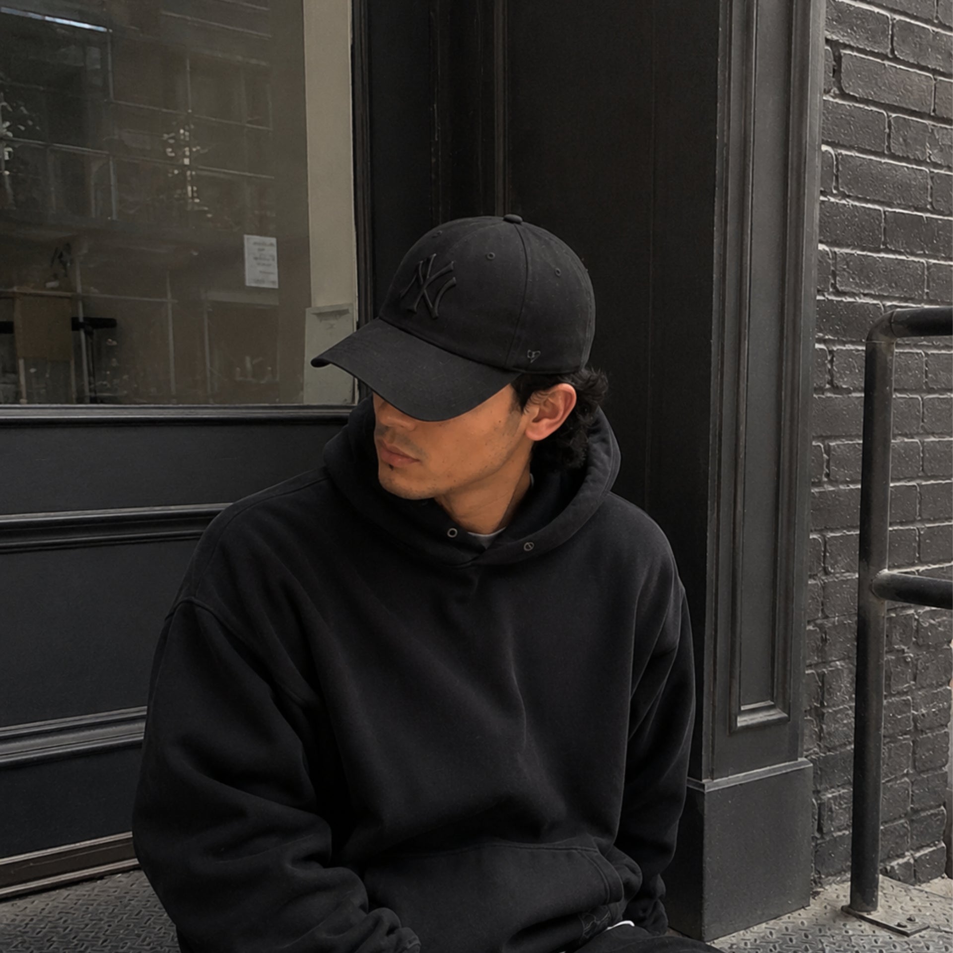 Man wearing all black New York Yankees adjustable hat outdoors