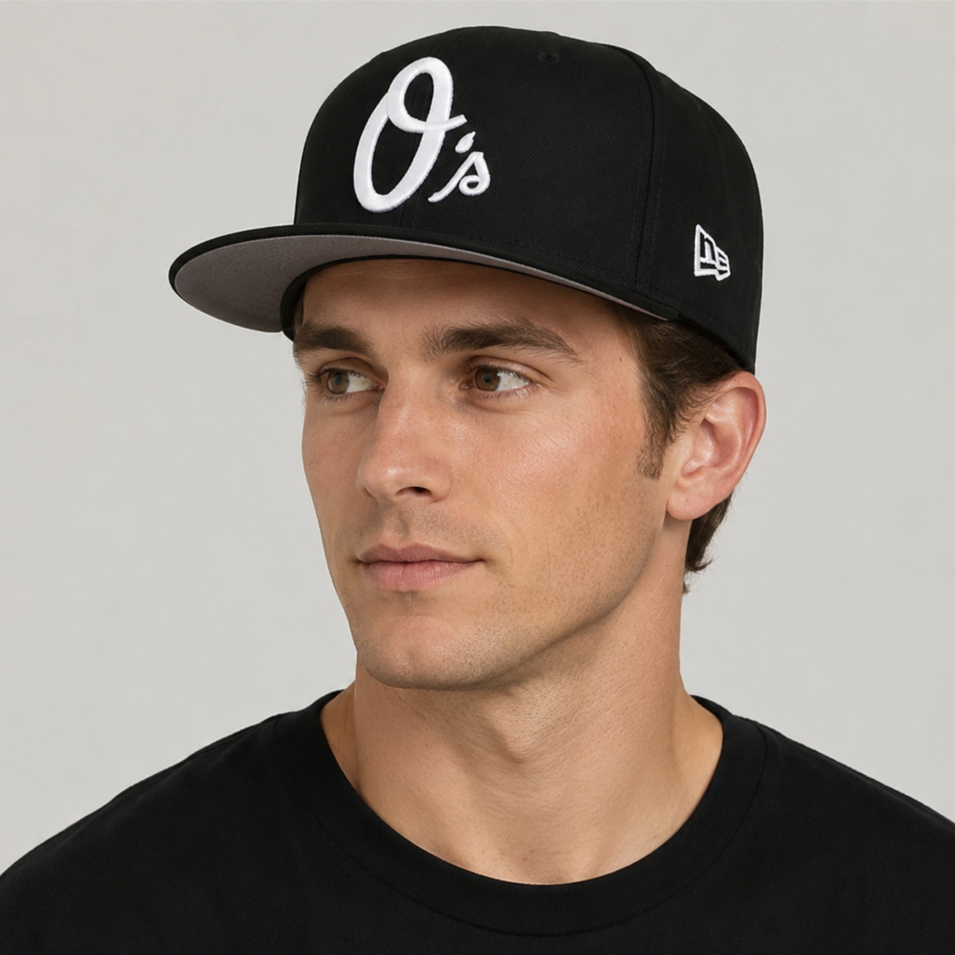 White male model wearing a black New Era Baltimore Orioles 59FIFTY fitted hat with white O’s logo and flat brim