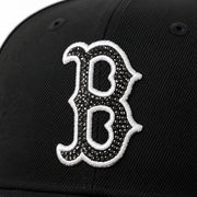 Close-up of a black baseball cap featuring a large embroidered Boston Red Sox letter 'B' logo embellished with rhinestones and outlined in white.