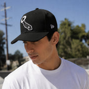 Man wearing a black cap with a white logo against a blue sky and trees background