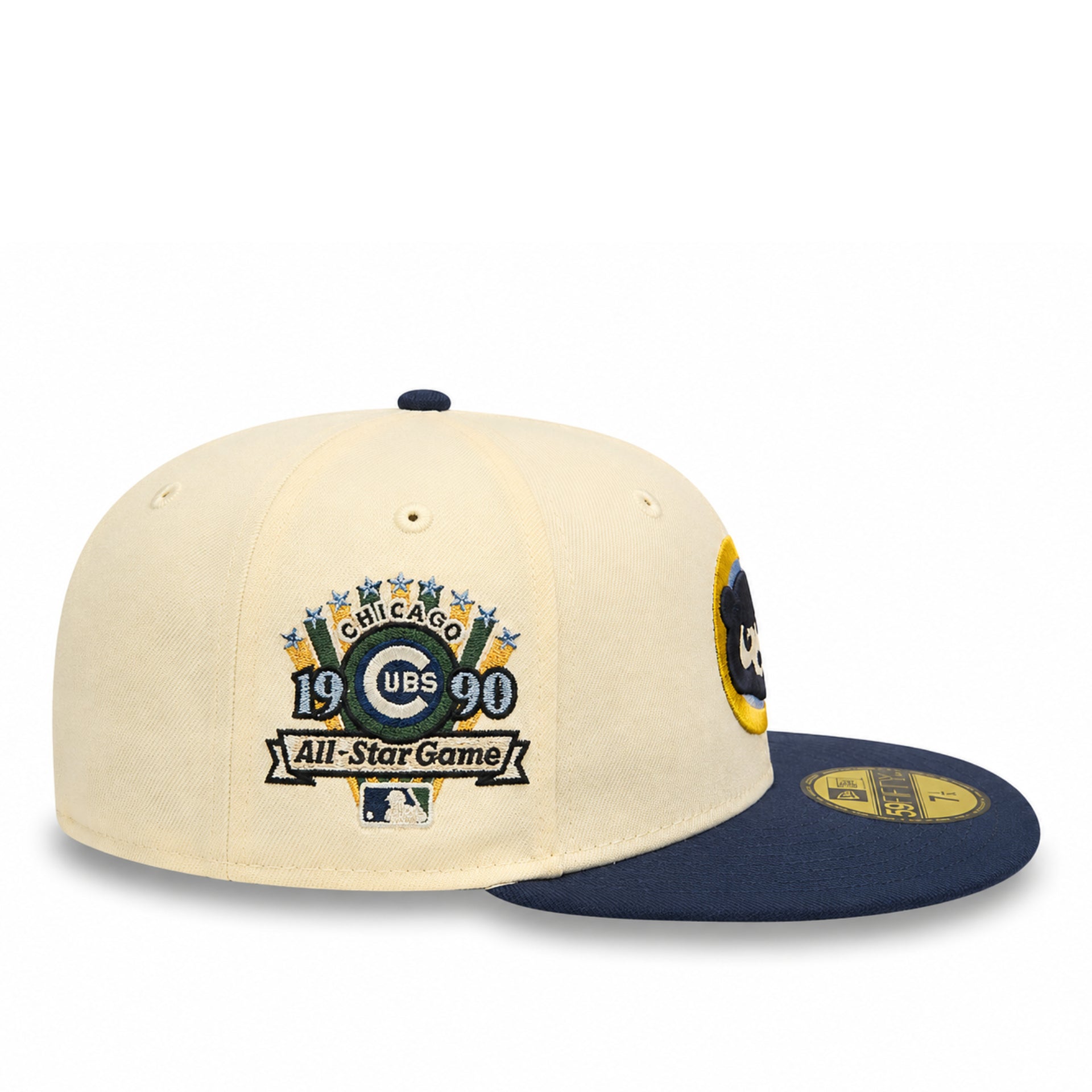 A cream-colored baseball cap with a navy blue flat brim, featuring a Chicago Cubs 1990 All-Star Game commemorative patch on the front and a gold size sticker on the brim.