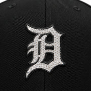 Close-up of a black baseball cap featuring a large embroidered letter 'D' patch covered in silver rhinestones, outlined in black.