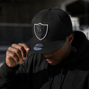 Person wearing a black cap with a Las Vegas Raiders logo, looking down.