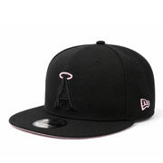 A black flat-brim baseball cap featuring a black embroidered Los Angeles Angels 'A' logo with a pink outline on the front, and a pink-outlined New Era flag logo on the side. The cap is photographed on a clean white background.