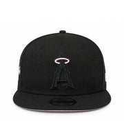 A black flat-brim baseball cap featuring an embroidered black Angels logo with a pink halo on the front, shown against a plain white background.