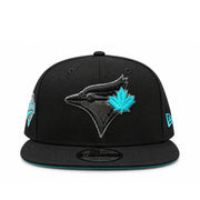 Angled front view of Toronto Blue Jays black 9FIFTY snapback featuring black embroidered bird logo, teal maple leaf and flat brim
